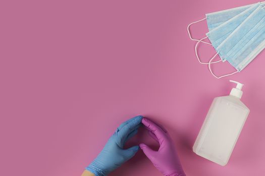 Protective medical white face mask and sanitizer gel on a pink background, success with a heart symbol made by a doctor's hands.  View from above. Virus Prevention Space for text. Close up, gorizontal orientation