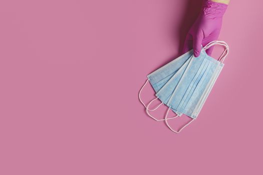 Doctor holds respiratory surgical face mask in hands pink medical gloves on pink background. Pandemic corona virus, insurance, airborne diseases, SARS, grippe. 
