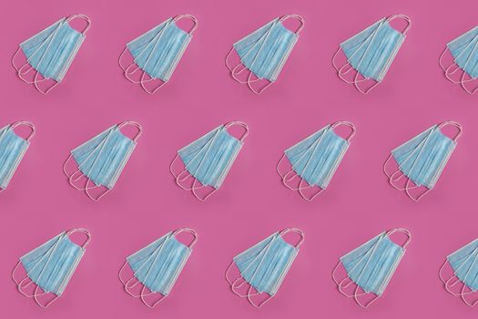 Many blue medical masks on the pink colored background to cover the mouth and nose for protection from virus and bacteria on a pink background. Epidemic concept. Regular pattern, flat lay.