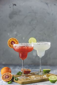 Frozen lime margarita and blood orange margarita cocktail mix in salt rimmed glasses garnished with slices of lime and orange. Focus on the citrus slice. Shallow depth of the field