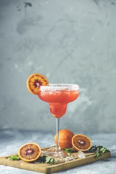 Red orange margarita cocktail with tequila, triple sec, orange juice, crushed ice and some salt on the rim of a glass, decorated with a citrus slice  Shallow depth of the field, light stone background