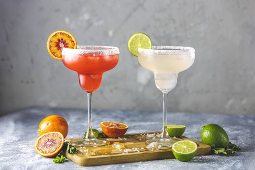 Frozen lime margarita and blood orange margarita cocktail mix in salt rimmed glasses garnished with slices of lime and orange. Focus on the citrus slice. Shallow depth of the field