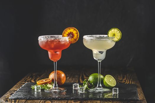 Frozen lime margarita and blood orange margarita cocktail mix in salt rimmed glasses garnished. Dark wooden background. Focus on the citrus slice. Shallow depth of the field.