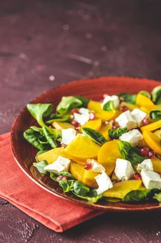 Healthy salad with persimmon, doucette (lambs-lettuce, cornsalad, field salad) and feta cheese on a red plate on a red background, superfoods vitamin persimmon salad