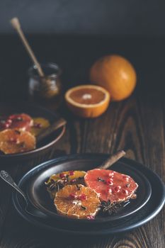 Orange dessert with wine honey or maple syrup and ginger spice, decorated pomegranate berries. Wonderfully sweet, rich and fresh food. Dark rustic background, copy space for you text.