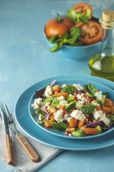 Blue plate of fresh superfoods healthy salad with red onion, tomatoes, doucette (lambs lettuce, corn salad, field salad) and feta cheese. Light blue surface