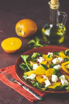 Healthy salad with persimmon, doucette (lambs-lettuce, cornsalad, feld salad) and feta cheese on a red plate on a red background. Superfoods Vitamin autumn or winter persimmon salad.