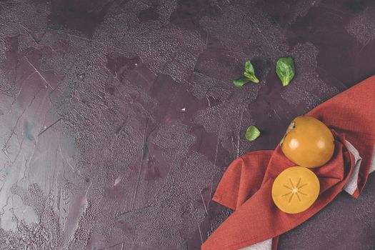 Healthy food background with persimmon and doucette (lambs-lettuce, cornsalad, field salad) with napkin on a red background, top view flat lay.