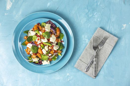 Blue plate of fresh superfoods healthy salad with red onion, tomatoes, doucette (lambs lettuce, corn salad, field salad) and feta cheese. Light blue surface, cutlery, top view, flat lay, copy space.