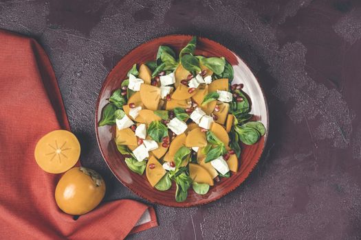 Healthy salad with persimmon, doucette (lambs-lettuce, cornsalad, feld salad) and feta cheese. Fitness food, superfoods vitamin persimmon salad. Top view, flat lay, copy space.