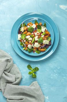 Blue plate of fresh superfoods healthy salad with red onion, tomatoes, doucette (lambs lettuce, corn salad, field salad) and feta cheese. Light blue surface, top view, flat lay, copy space.