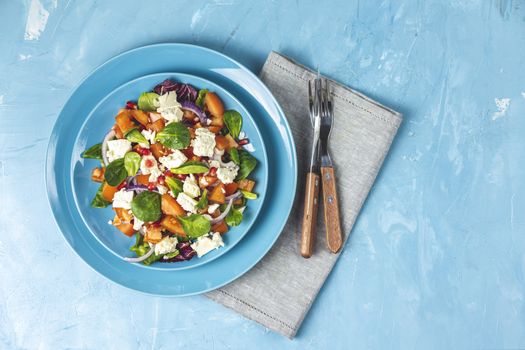 Blue plate of fresh superfoods healthy salad with red onion, tomatoes, doucette (lambs lettuce, corn salad, field salad) and feta cheese. Light blue surface, top view, flat lay, copy space.