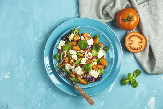 Blue plate of fresh superfoods healthy salad with red onion, tomatoes, doucette (lambs lettuce, corn salad, field salad) and feta cheese. Light blue surface, top view, flat lay, copy space.