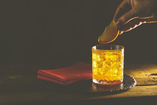 Woman hand decorate orange slice alcoholic cocktail negroni of the glass. Drink with gin, campari martini rosso and orange, an italian cocktail, an aperitif, first mixed in Firenze, Italy, in 1919