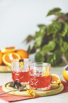 Two glasses of chocolate red orange negroni, an italian cocktail, an aperitif, first mixed in Firenze, Italy, in 1919, alcoholic bitter cocktail served by ingredients on the light gray table.