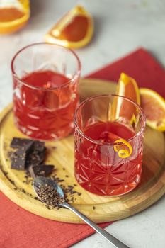 Two glasses of chocolate red orange negroni, an italian cocktail, an aperitif, first mixed in Firenze, Italy, in 1919, alcoholic bitter cocktail served by ingredients on the light gray table.