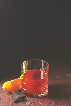 Glass of chocolate red orange negroni, an italian cocktail, an aperitif, first mixed in Firenze, Italy, in 1919, alcoholic bitter cocktail served by ingredients on the dark claret bordeaux table