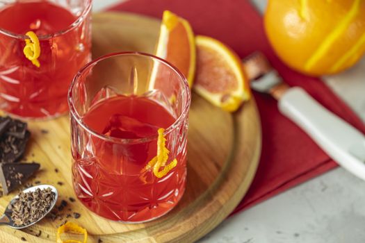Two glasses of chocolate red orange negroni, an italian cocktail, an aperitif, first mixed in Firenze, Italy, in 1919, alcoholic bitter cocktail served by ingredients on the light gray table.