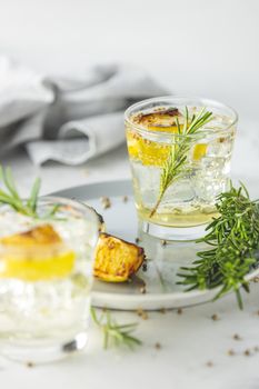 Glasses of Gin and Tonic with Charred Lemon, Rosemary and Coriander is a flavors are perfectly balanced refreshing cocktail. on light background, close up surrounded ingredients, selective focus