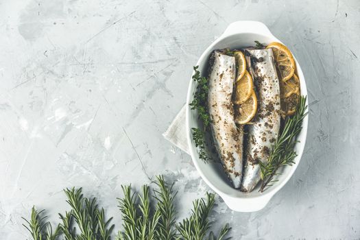 Mackerels served on white dish with lemon, thyme, rosemary and spices. Raw marinated fishes on light gray surface. Seafood background