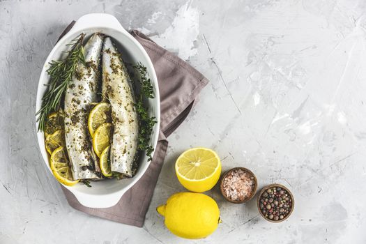 Mackerels served on white dish with lemon, thyme, rosemary and spices. Raw marinated fishes on light gray surface. Seafood background.