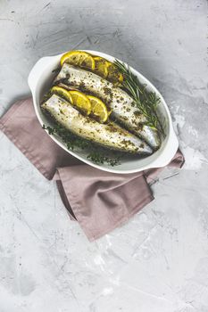 Mackerels served on white dish with lemon, thyme, rosemary and spices. Raw marinated fishes on light gray surface. Seafood background
