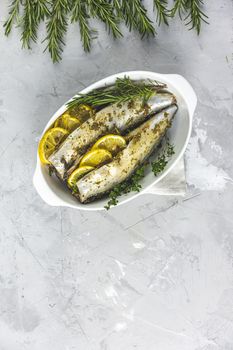 Mackerels served on white dish with lemon, thyme, rosemary and spices. Raw marinated fishes on light gray surface. Seafood background.