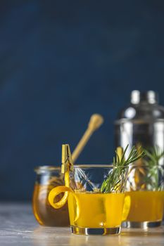 Two glasses of honey bourbon cocktail with rosemary simple syrup or homemade whiskey sour cocktail drink with orange and rosemary decoration orange peel, jar of honey  and bartender tools