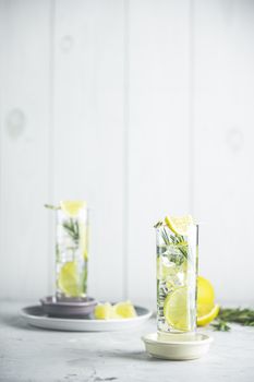 Refreshing lemon lime drink with ice cubes in glass goblets against a light gray background. Summer fresh lemon soda cocktail with rosemary, selective focus