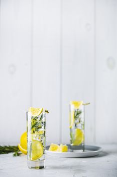 Two glasses of refreshing lemon lime drink with ice cubes in glass goblets against a light gray background. Summer fresh lemon soda cocktail with rosemary, selective focus