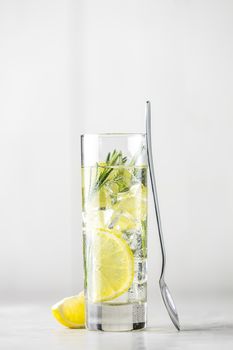 Refreshing lemon lime drink with ice cubes in glass goblets against a light gray background. Summer fresh lemon soda cocktail with rosemary, selective focus.