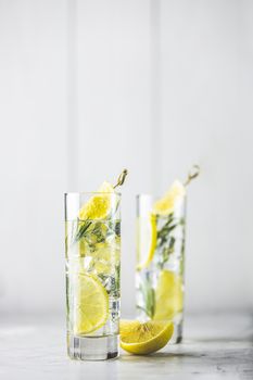 Refreshing lemon lime drink with ice cubes in glass goblets against a light gray background. Summer fresh lemon soda cocktail with rosemary, selective focus