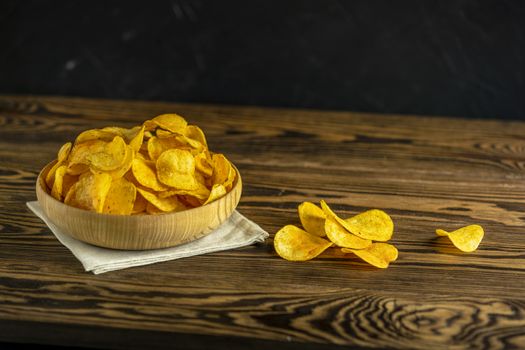 Potato chips in bowl on a wooden background. Salty crisps scattered on a table.