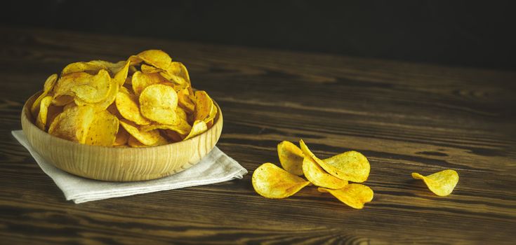 Potato chips in bowl on a wooden background. Salty crisps scattered on a table.