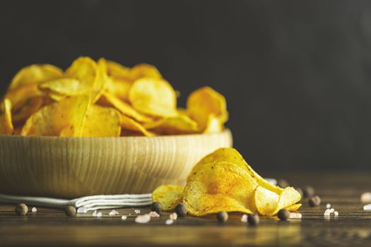 Potato chips in bowl on a wooden background. Salty crisps scattered on a table.