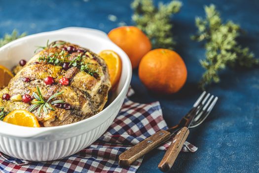 Color of 2020 year. Classic Blue, food trendy background. Roasted pork in white dish, christmas baked ham with cranberries, tangerines, thyme, rosemary, garlic on dark table surface