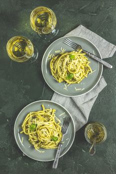 Spaghetti pasta bucatini with pesto sauce and parmesan. Italian traditional perciatelli pasta by genovese pesto sauce in two gray dishes, top view, flat lay, served with wine