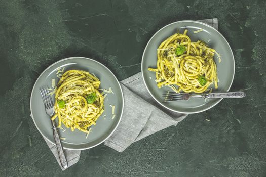 Spaghetti pasta bucatini with pesto sauce and parmesan. Italian traditional perciatelli pasta by genovese pesto sauce in two gray dishes, top view, flat lay