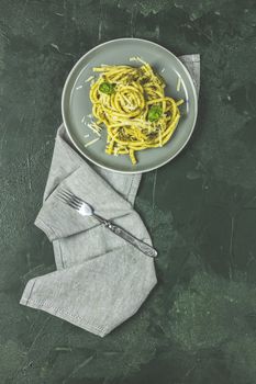 Spaghetti pasta bucatini with pesto sauce and parmesan. Italian traditional perciatelli pasta by genovese pesto sauce in gray dish. Flat lay on dark green surface.