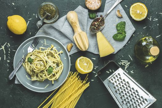 Italian traditional perciatelli pasta by genovese pesto sauce in gray dish served with ingradients on dark green concrete table. Flat lay on dark green surface	