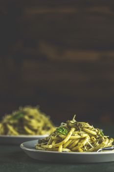 Spaghetti pasta bucatini with pesto sauce and parmesan. Italian traditional perciatelli pasta by genovese pesto sauce  in two ray dishes. Dark green concrete surface, rustic style, close up