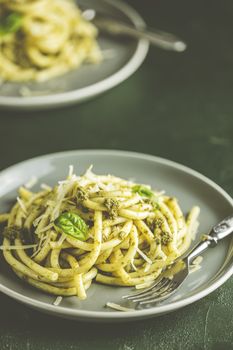 Spaghetti pasta bucatini with pesto sauce and parmesan. Italian traditional perciatelli pasta by genovese pesto sauce  in two ray dishes. Dark green concrete surface, rustic style, close up