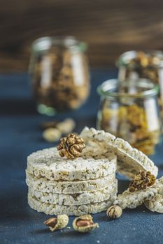 Stack of rice cakes. American puffed rice cakes. Healthy snacks with almonds, raisins, peanuts, pistachios in glass jars on classic blue concrete surface. Close up.