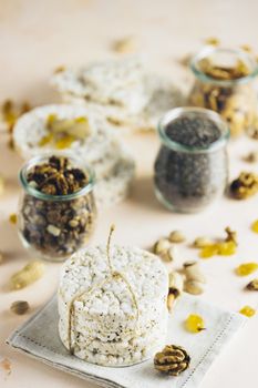 American puffed rice cakes. Healthy snacks with almonds, raisins, peanuts, pistachios in glass jars on light pink concrete surface.