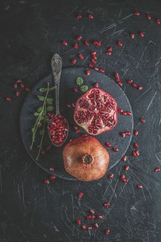 Fresh juicy pomegranate - whole and cut on a black vintage background, top view, horizontal, with copy space