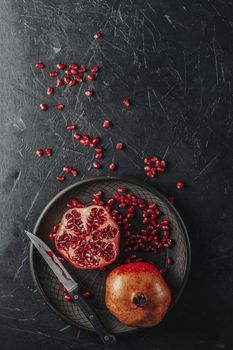 Fresh juicy pomegranate - whole and cut on a black vintage background, top view, horizontal, with copy space