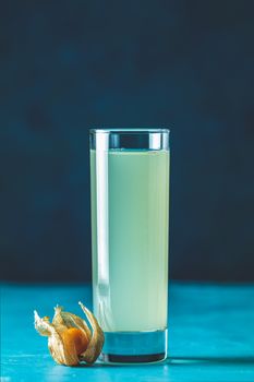 Alcoholic cocktail with Ouzo greek anise brandy or Arabic alcohol drink Raki in highball glass, decorated Physalis peruviana and brown sugar on blue concrete surface.