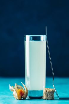 Alcoholic cocktail with Ouzo greek anise brandy or Arabic alcohol drink Raki in highball glass, decorated Physalis peruviana and brown sugar on blue concrete surface.