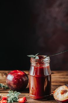 Homemade DIY natural canned hot plum sauce chutney with chilli or tkemali in glass jar standing on wooden table with ingredients — plum, salt, pepper,  herbs, selective focus