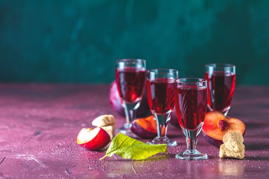 Plums strong alcoholic drink in shots. Hard liquor, slivovica, plum brandy or plum vodka with ripe plums on dark green and  claret bordeaux concrete surface.